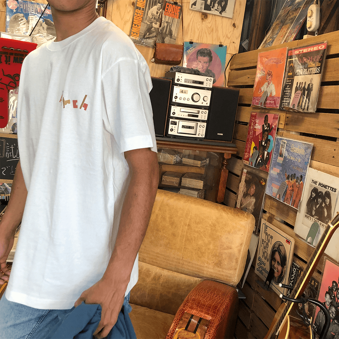 アーチの白いロゴｔシャツを着て歩く人